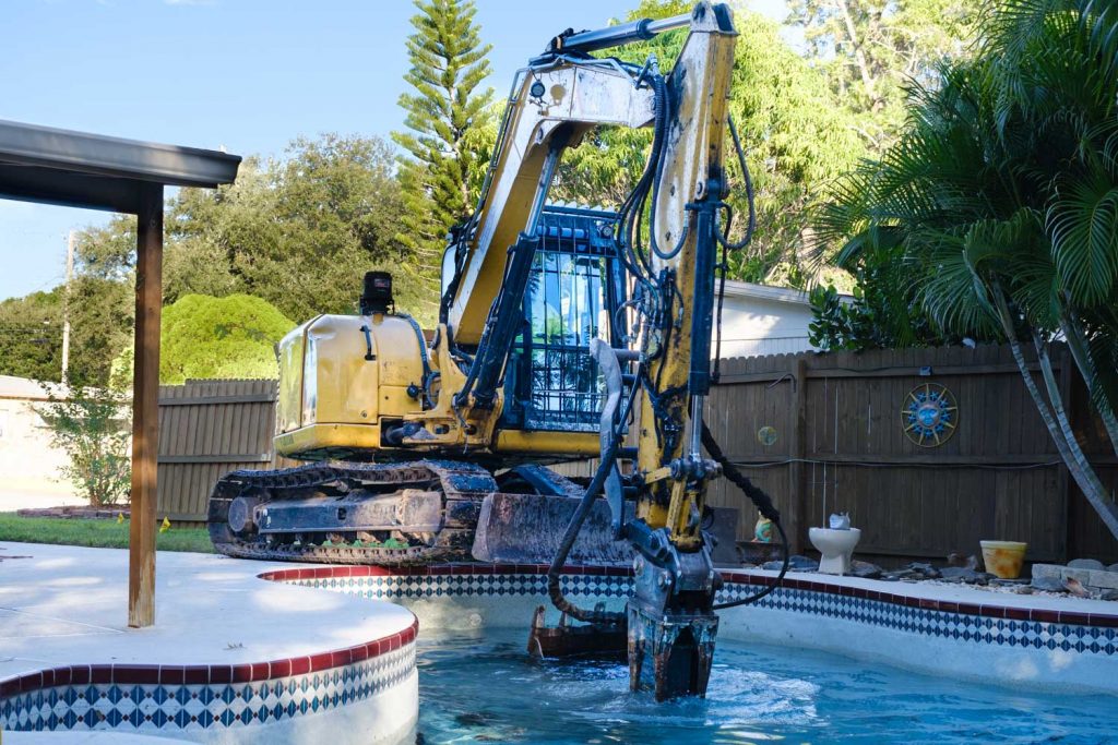 excavator breaks pool with demolition hammer